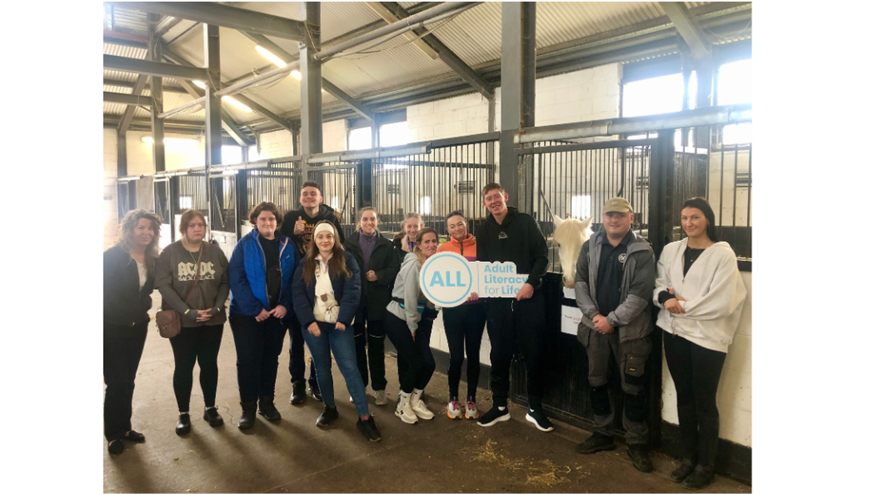 Group of people posing in a stable, holding an 